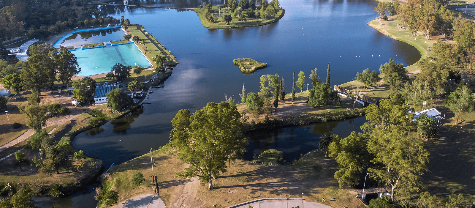 Vista aerea del parque municipal, se ve la vegetación, laguna y pileta.